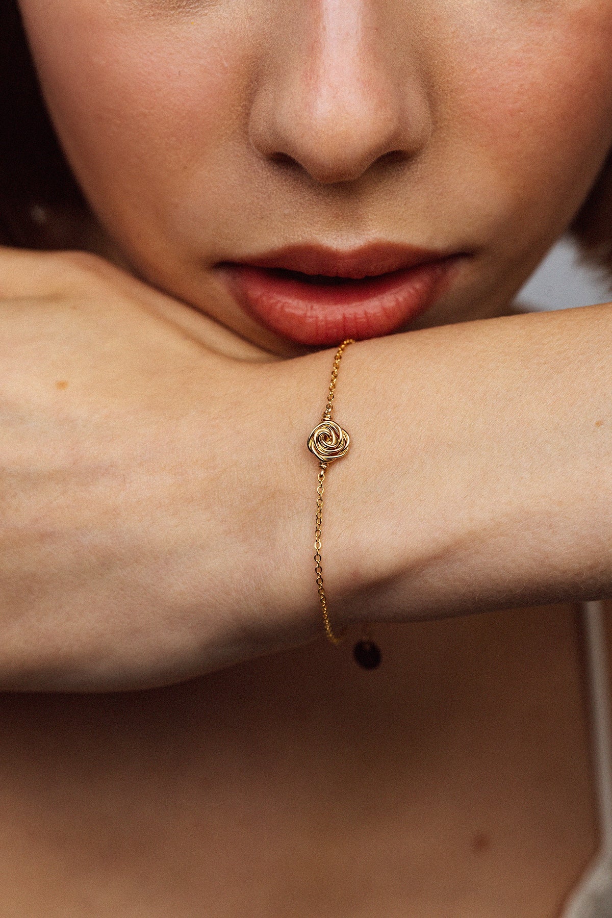 Pulsera Rosa puesta en la muñeca, rosa dorada sobre cadena fina