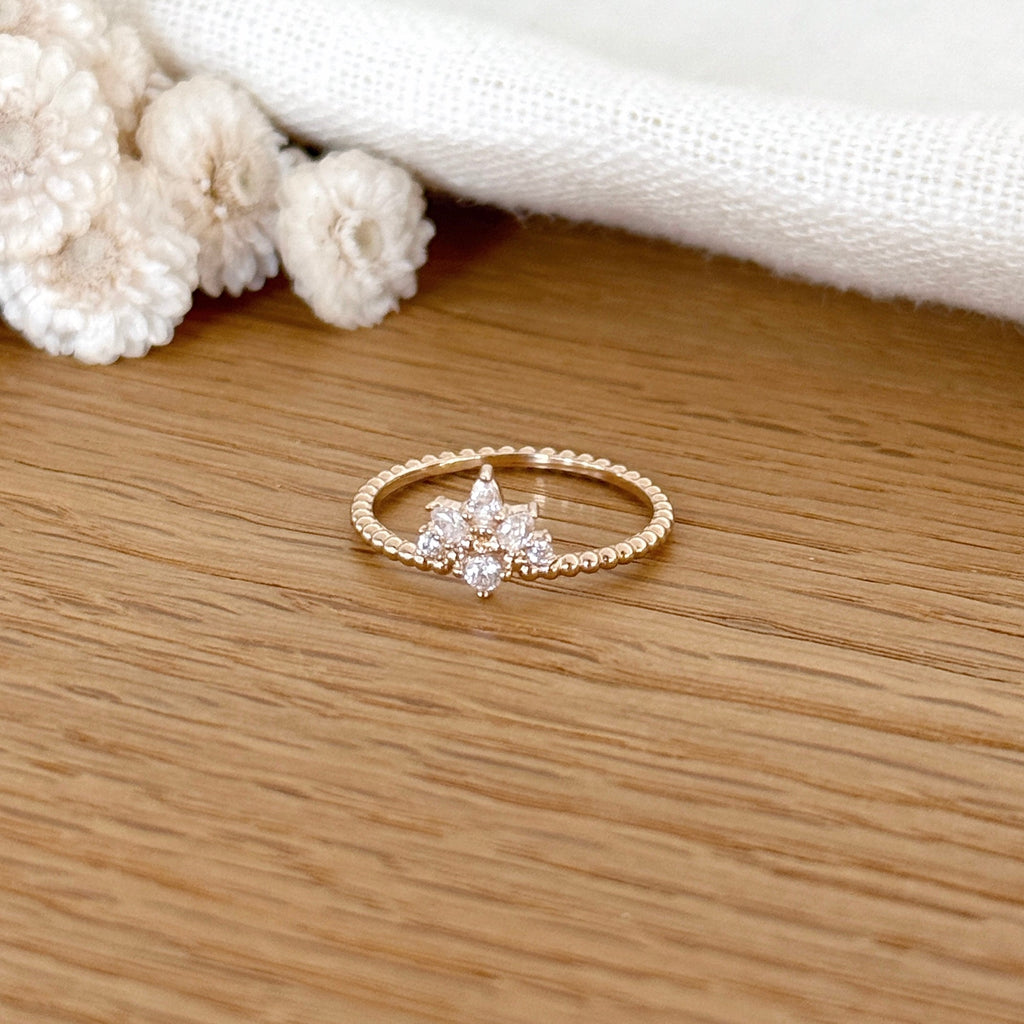 Instants Plaisirs – Bague "Adam" Plaqué Or, bague dorée avec des strass en forme de fleur, posée sur une table en bois