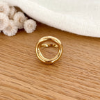 Instants Plaisirs – Bague "Orma" Acier, bague dorée avec un cercle irrégulier sur une surface en bois