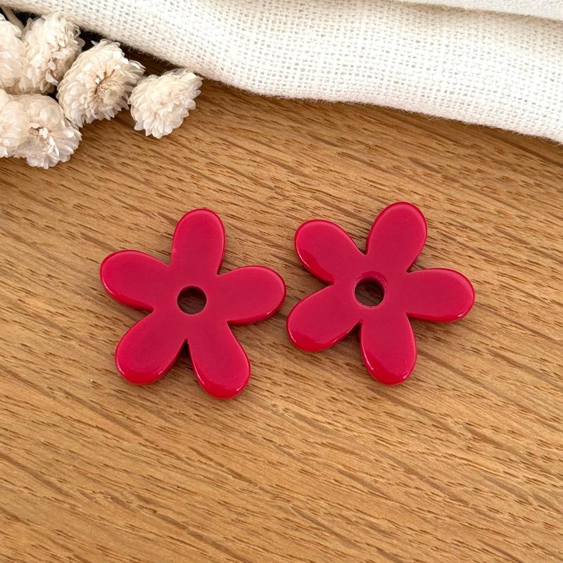 Instants Plaisirs – Fleurs "Maria" Acétate, deux fleurs en résine rouge posées sur une table en bois