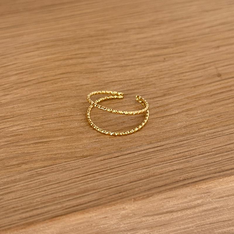 Instants Plaisirs – Bague "Lia" Acier, bague dorée à double anneau texturé posée sur une surface en bois