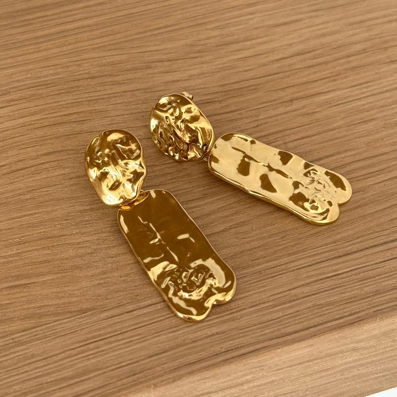 Instants Plaisirs – Boucles D'Oreilles "Rena" Acier, boucles d'oreilles dorées texturées posées sur une surface en bois clair