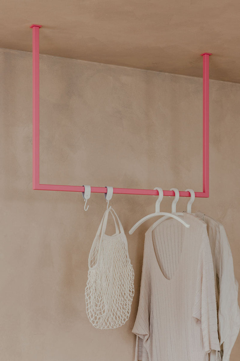 Kleiderstange RUBI in minimalistischem Design mit einem rosa Gestell, ideal für Ankleidebereiche, mit Kleidern und Tasche.
