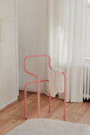 Minimalist Herrendiener in Rosa mit einem Kleidungsstück auf der Rückenlehne, ideal für Schlafzimmer.