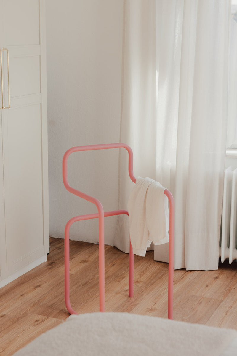 Minimalist Herrendiener in Rosa mit einem Kleidungsstück auf der Rückenlehne, ideal für Schlafzimmer.
