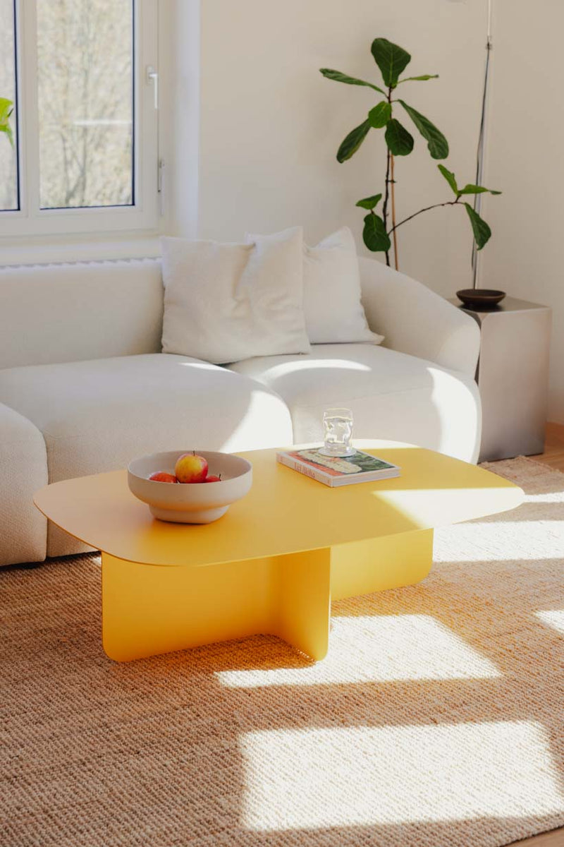 Heller Couchtisch Livia in modernem Design mit frischem Gelb, dekoriert mit Obstschale und Buch auf einem eleganten Teppich.