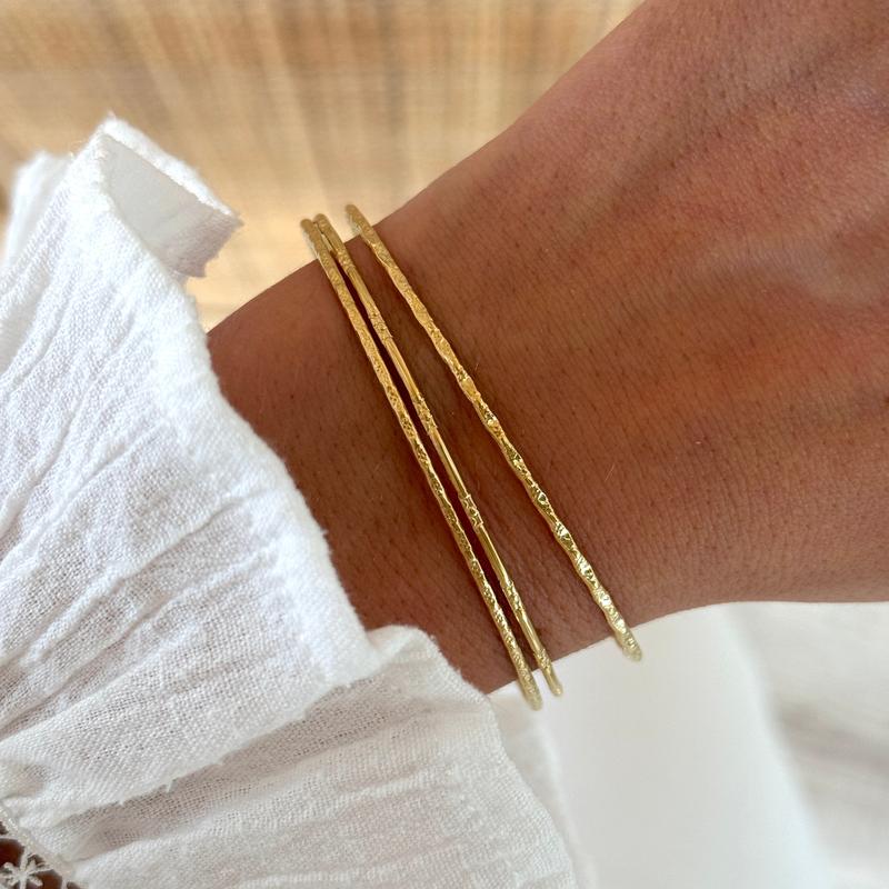 Instants Plaisirs – Joncs "Misa" Acier, trois bracelets dorés texturés portés au poignet d'une femme