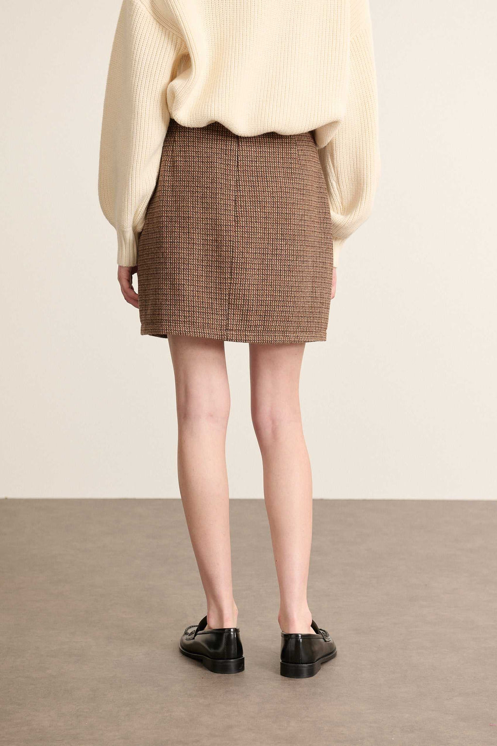 Coloris marron, la mini jupe BOWEN est fabriquée en laine et polyester avec un tissu esprit pied de poule. 