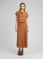 An'ge – Top Kiline Daim, Model in einem langen braunen Kleid mit braunen Sandalen