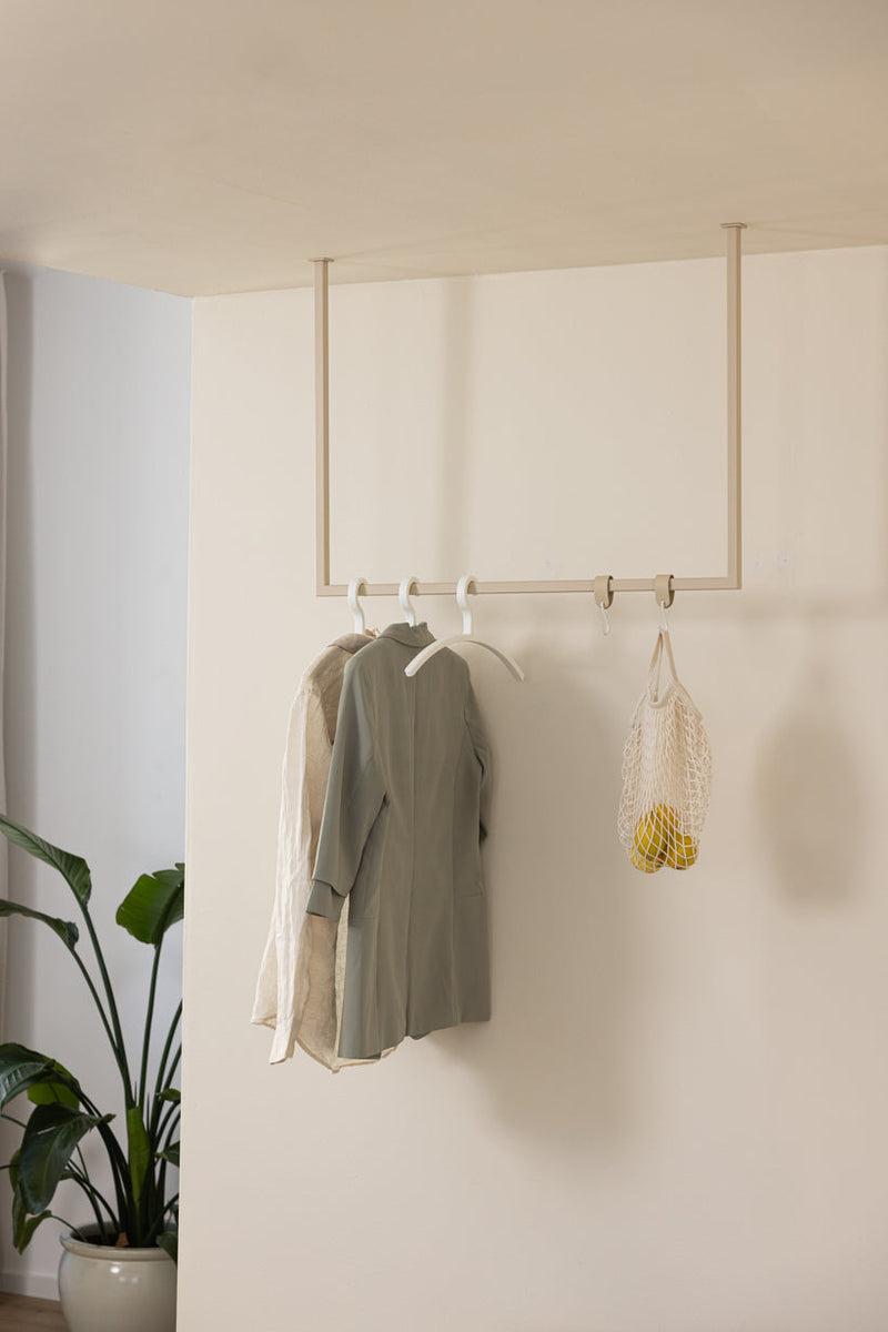 Kleiderstange RUBI mit Kleidung und Netztasche an einer Wand in einem modernen Ankleidebereich.