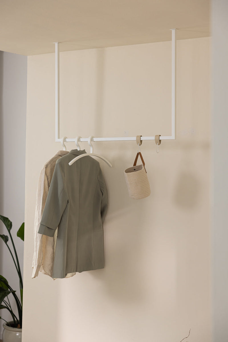 Kleiderstange RUBI mit eleganter Kleidung und dekorativem Behälter an einem minimalistischen Wandhaken.