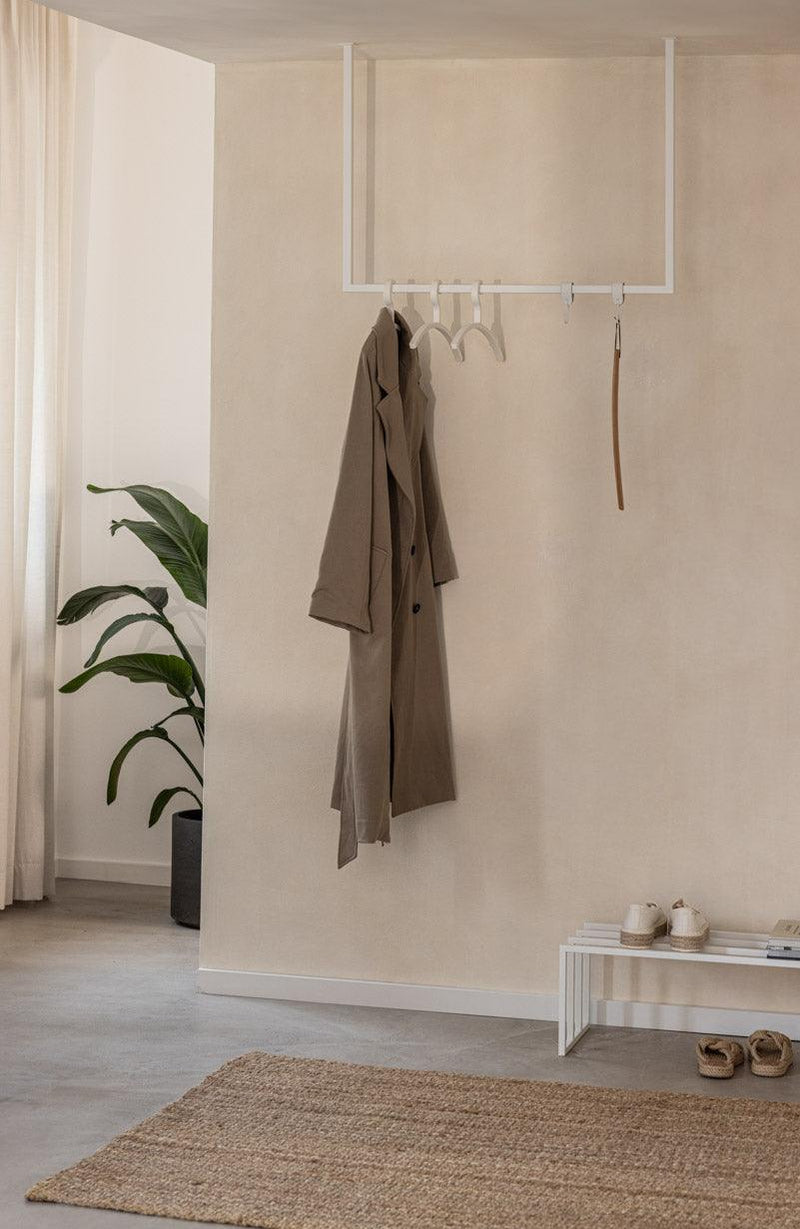 Moderne Kleiderstange RUBI mit minimalistischer Form, hält elegant einen Mantel in einem stilvollen Ankleidebereich.