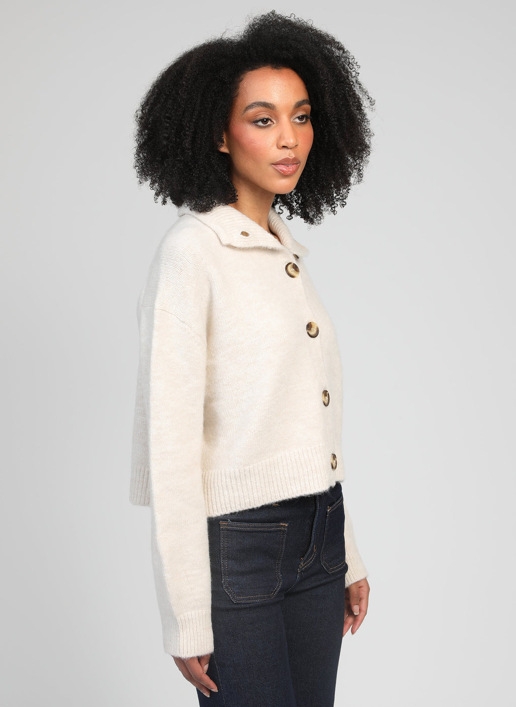 An'ge – Gilet Lakeyla Ecru, mannequin femme de profil portant un cardigan en maille crème et un jean
