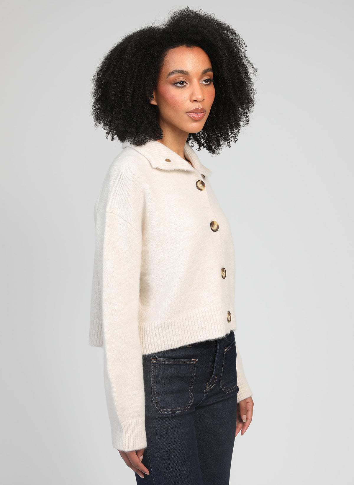 An'ge – Gilet Lakeyla Ecru, mannequin femme de profil portant un cardigan en maille crème et un jean