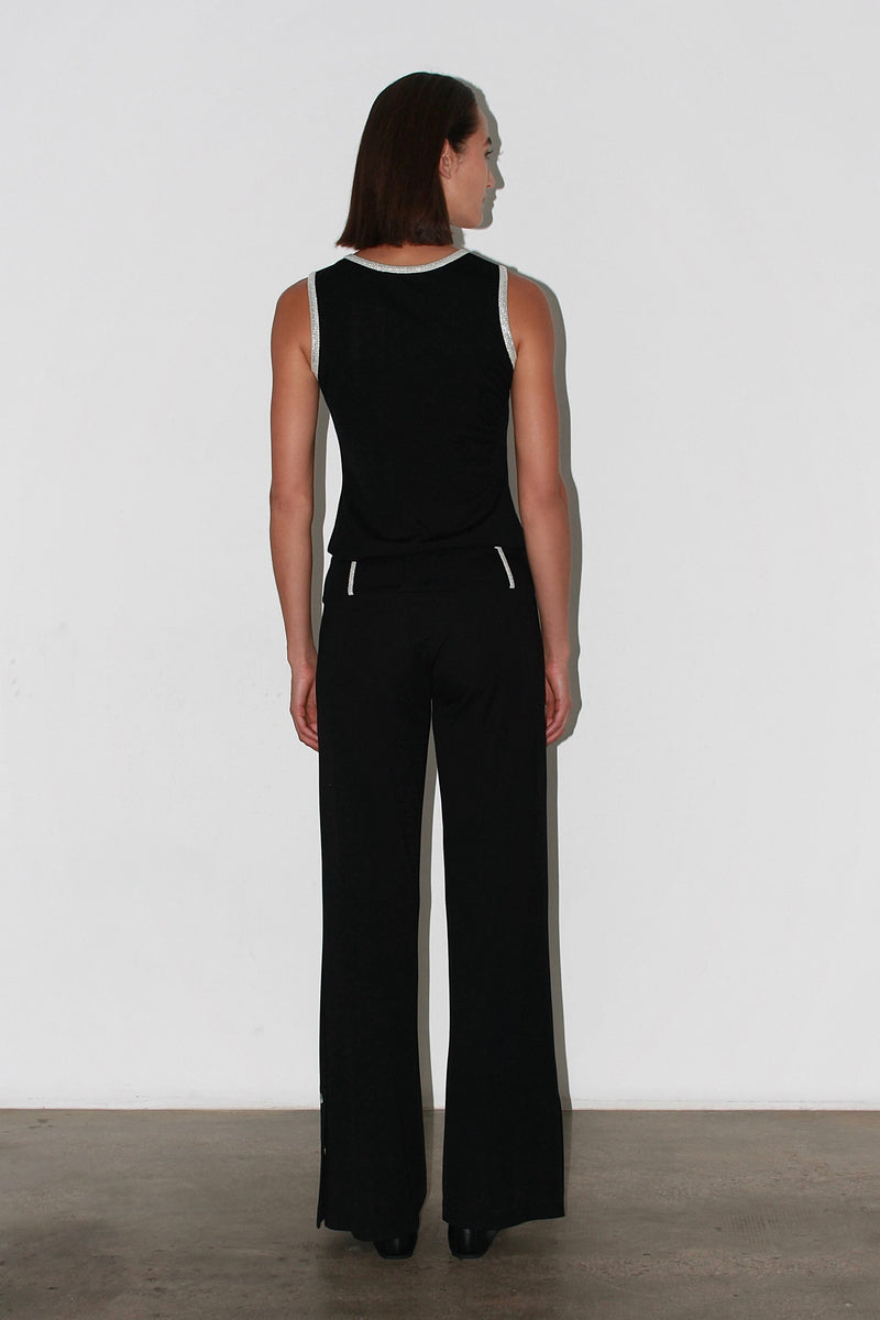 Vista frontal de tres cuartos: elegantes pantalones negros con detalles de botones metálicos en la cintura.