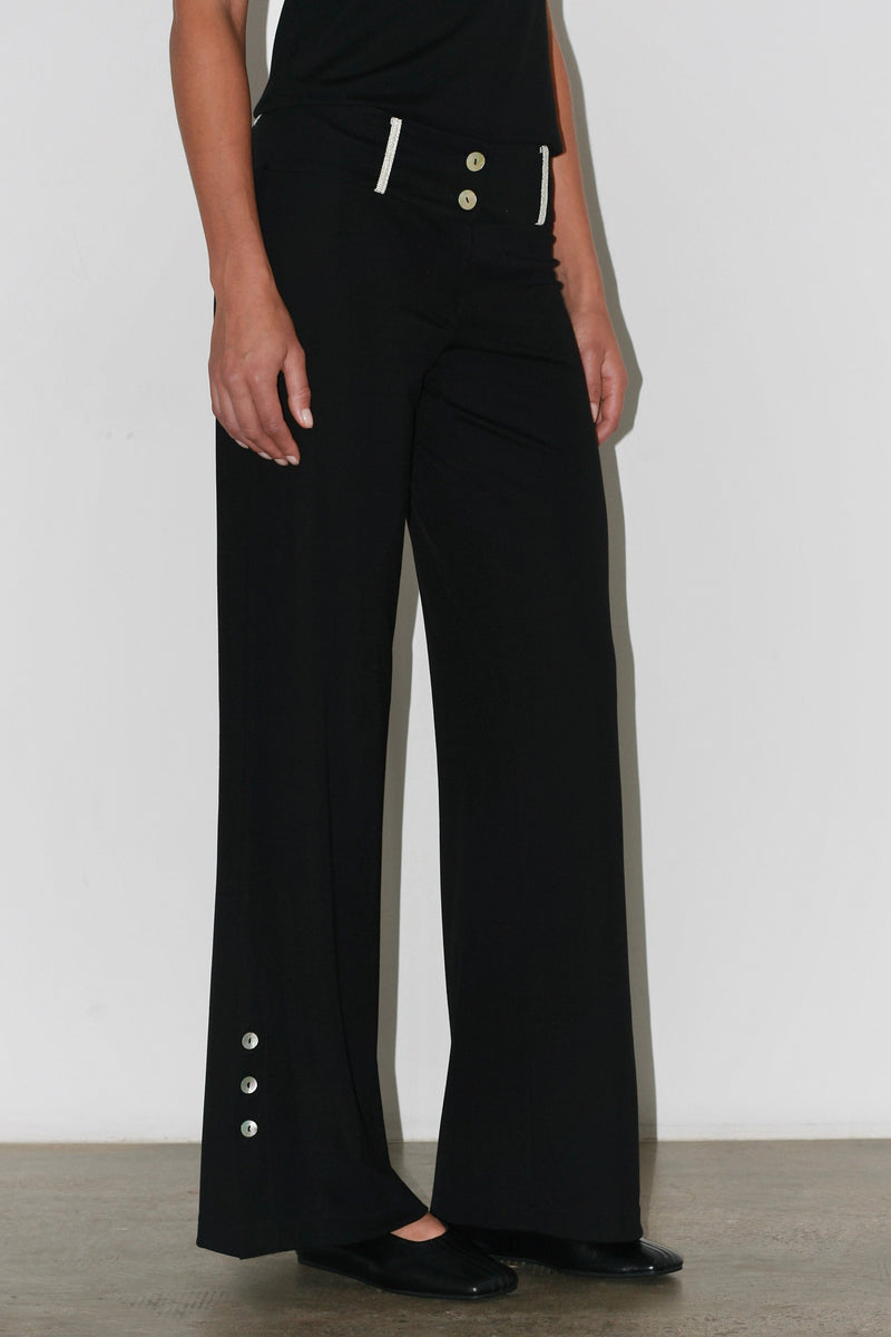 Primer plano de los pantalones Zeynep: corte de talle alto con costuras delanteras y adornos de botones plateados.