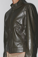 Primer plano lateral: chaqueta de cuero verde oscuro con costuras detalladas y acabado brillante.