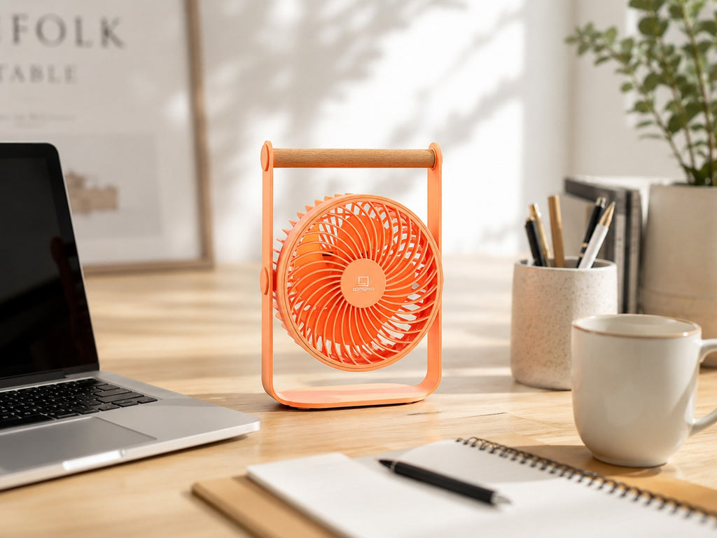 Gingko Design – Tragbarer Ventilator Lyra - Pfirsich, ein oranger Ventilator auf einem Holzschreibtisch mit einem Laptop