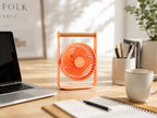 Gingko Design – Tragbarer Ventilator Lyra - Pfirsich, ein oranger Ventilator auf einem Holzschreibtisch mit einem Laptop