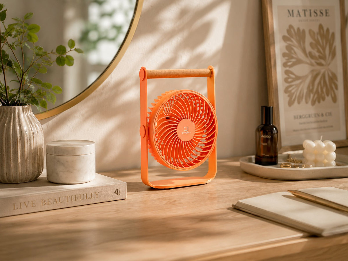 Gingko Design – Tragbarer Ventilator Lyra - Pfirsich, ein oranger Ventilator auf einem Holztisch, in einem dekorierten Raum