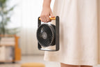 Gingko Design – Ventilador Portátil Lyra - Gris Espacial, una persona con vestido claro sostiene un ventilador portátil gris y madera