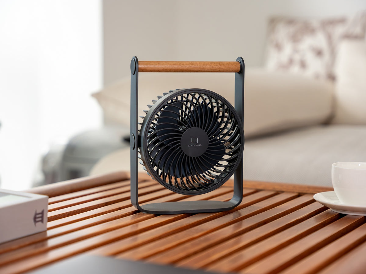Gingko Design – Ventilador Portátil Lyra - Gris Espacial, pequeño ventilador negro y madera colocado sobre una mesa de madera