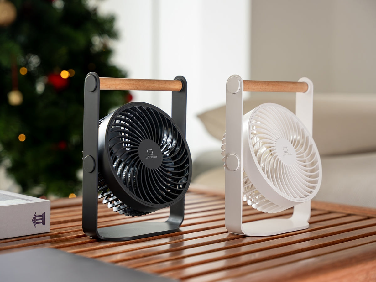 Gingko Design – Ventilador Portátil Lyra - Gris Espacial, dos ventiladores de mesa, uno negro y uno blanco, colocados sobre una mesa de madera