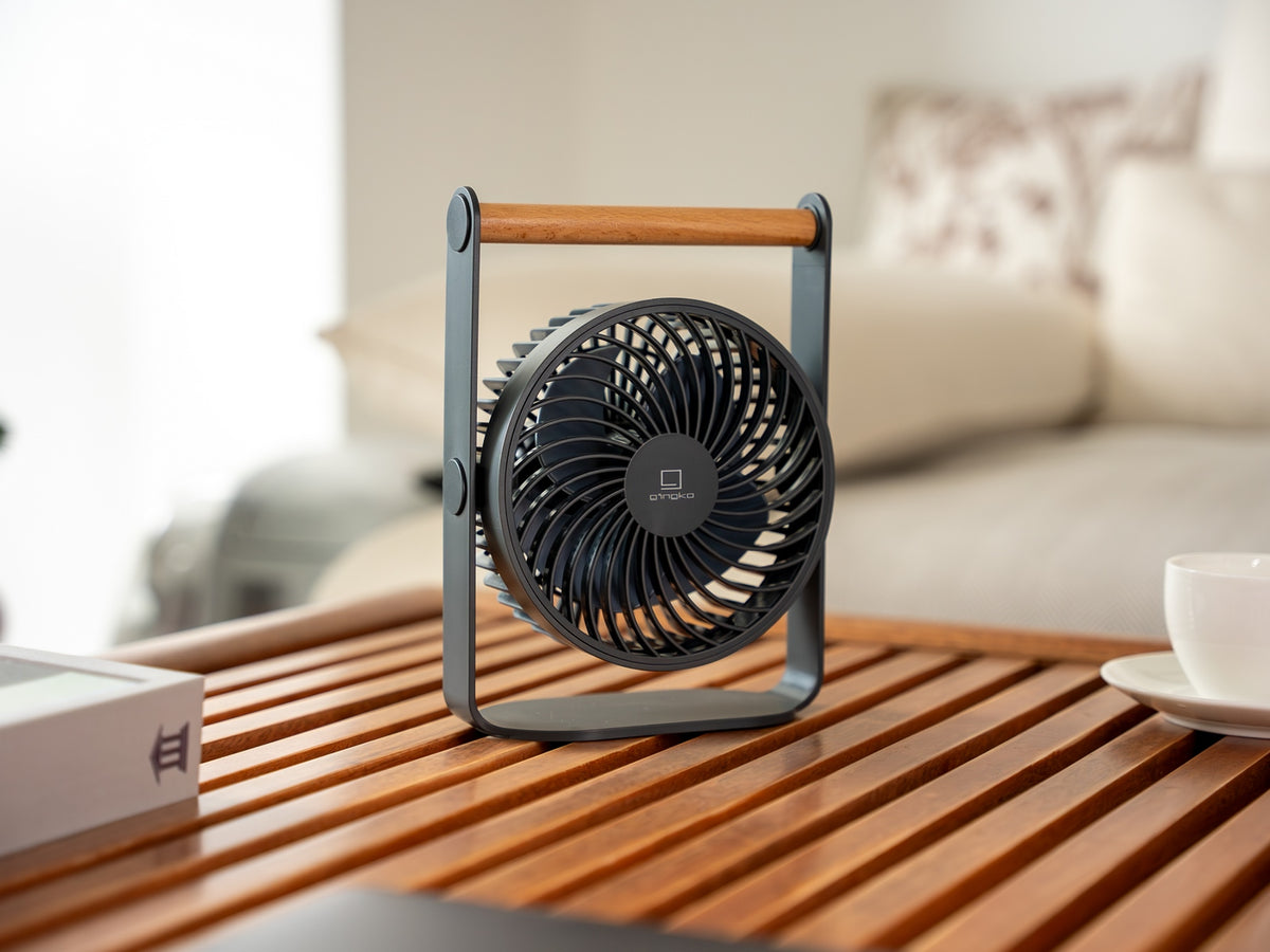 Gingko Design – Ventilador Portátil Lyra - Gris Espacial, un ventilador de mesa negro y madera sobre una mesa de madera