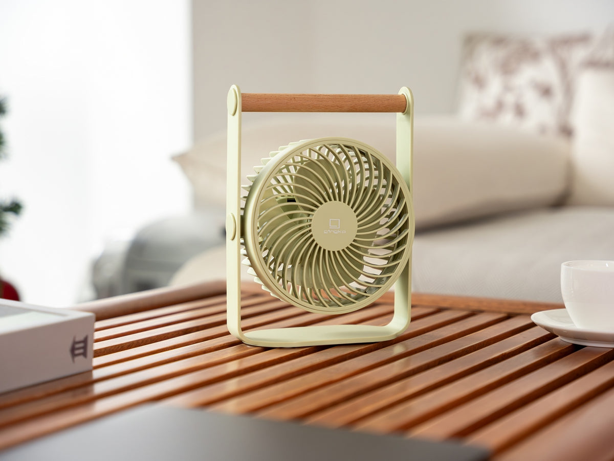 Gingko Design – Ventilador Portátil Lyra - Gris Espacial, ventilador de mesa verde claro con asa de madera sobre una mesa de centro