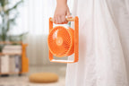 Gingko Design – Tragbarer Ventilator Lyra - Pfirsich, oranger tragbarer Ventilator, von einer Person im weißen Kleid gehalten