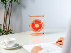 Gingko Design – Tragbarer Ventilator Lyra - Pfirsich, oranger Tischventilator auf einem weißen Schreibtisch stehend