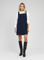 An'ge – Robe Courte Maleo Marine, mannequin blonde portant une robe chasuble bleu marine sur chemise blanche