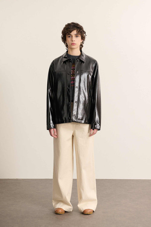 Mannequin femme de face portant une veste courte en vinyle noir, coupe droite avec poches plaquées et allure affirmée.