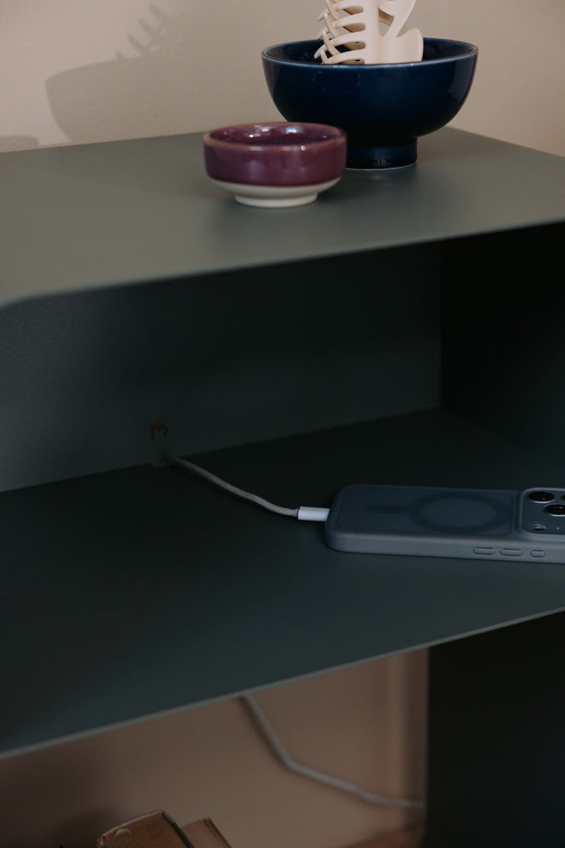 Stehender Nachttisch mit minimalistischem Design, Ladeschale und dekorativen Schalen auf der Ablage.