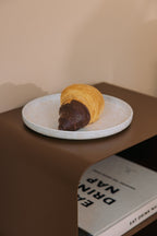 Stehender Nachttisch mit einer Servierplatte und einem Schokoladen-Croissant darauf.