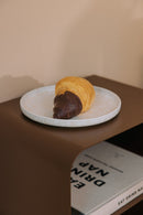 Stehender Nachttisch mit einer Servierplatte und einem Schokoladen-Croissant darauf.