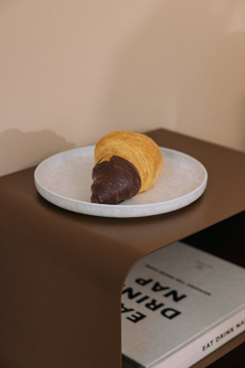 Stehender Nachttisch mit einer Servierplatte und einem Schokoladen-Croissant darauf.