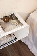 Hängender Nachttisch NELIO mit modernen Design-Elementen und minimalistischer Oberfläche, dekoriert mit Büchern und einer Vase.