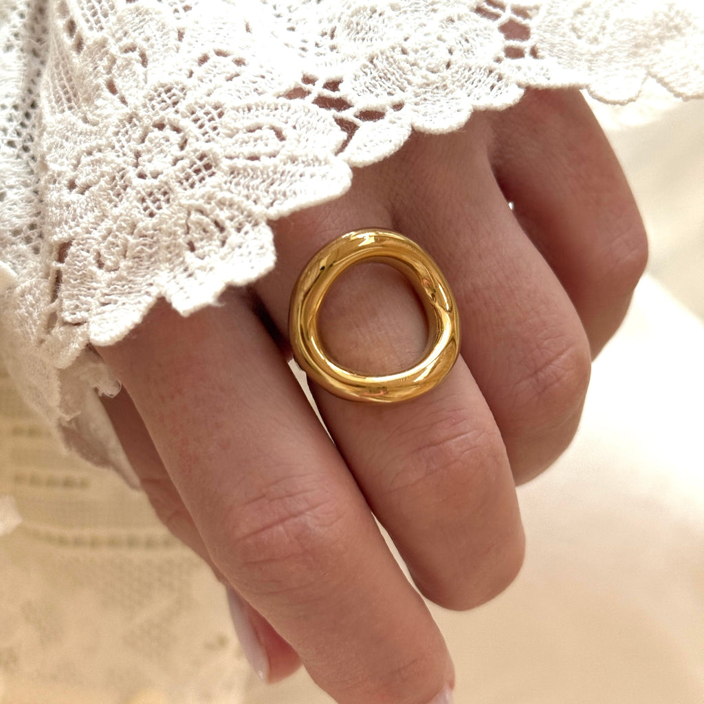 Instants Plaisirs – Bague "Orma" Acier, bague dorée portée au doigt d'une femme, avec une manche en dentelle blanche