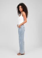An'ge – Pantalón Pafli Azul, modelo mujer de perfil con camiseta de tirantes blanca y vaquero azul claro