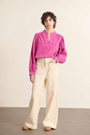 Mannequin femme de face portant une blouse ample coloris fuchsia, en toile sergée de coton, col rond et manches longues.