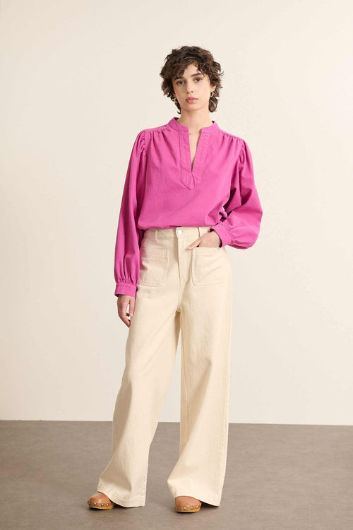 Mannequin femme de face portant une blouse ample coloris fuchsia, en toile sergée de coton, col rond et manches longues.