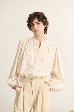 Mannequin femme de face portant une blouse ample coloris écru en dentelle, coupe droite avec col rond et manches longues.