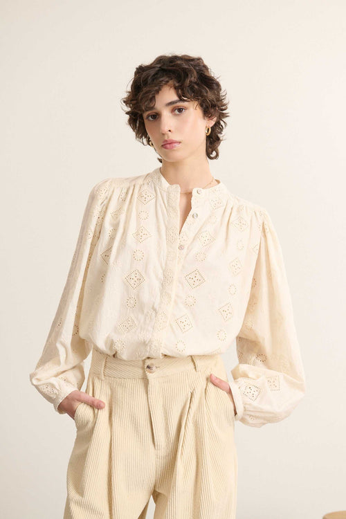 Mannequin femme de face portant une blouse ample coloris écru en dentelle, coupe droite avec col rond et manches longues.