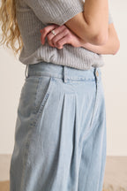 Pantalon bleu en chambray, silhouette fluide avec plis devant, jambes larges et modernes