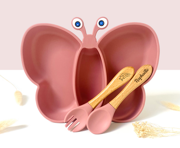 Plato Léon la Mariposa: juego de vajilla infantil rosa con forma de mariposa y sobre ella se colocan utensilios de madera grabados “Raphaëlle”.