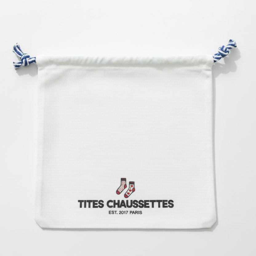 Pochon coton pour ranges ses Tites Chaussettes. Fond blanc, imprimé chaussettes à motifs bleu/rouge. Fermeture par lien coulissant blanc/bleu. 