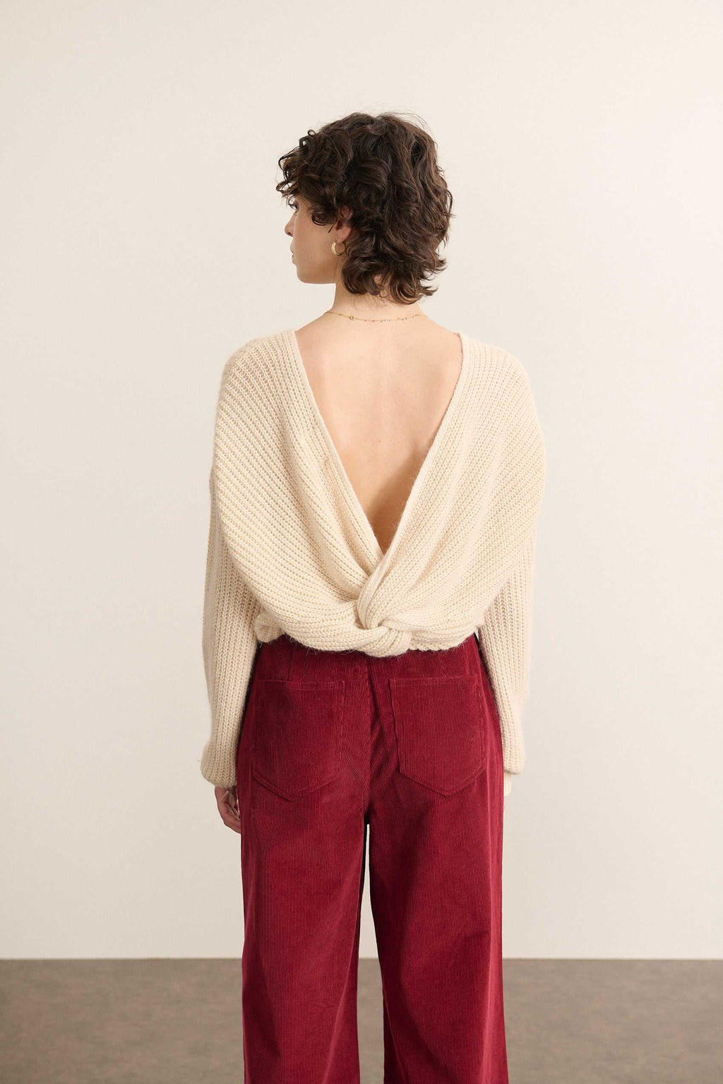Vue arrière du pull beige, décolleté profond en V orné d’un nœud fixe et coupe droite légèrement ajustée.