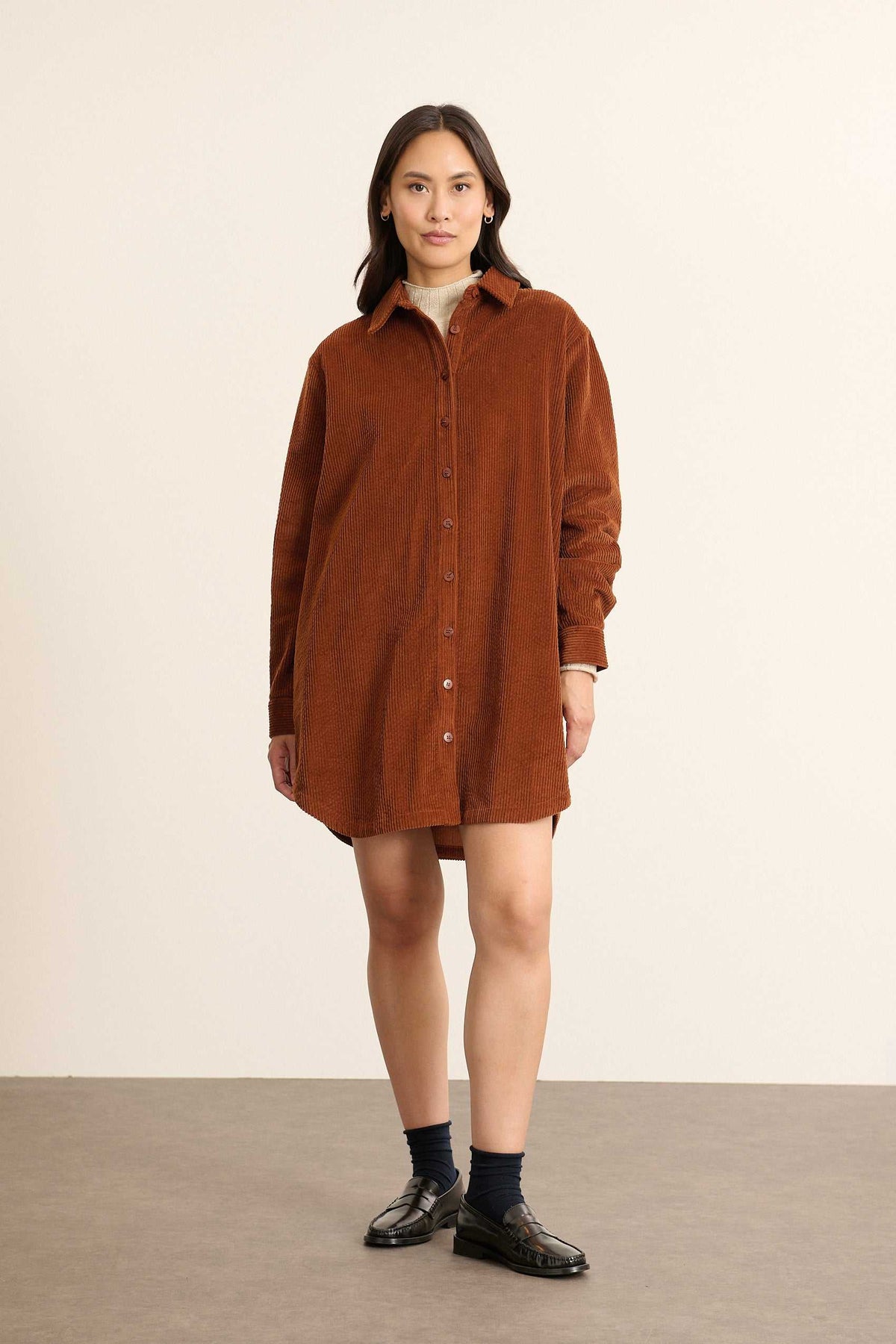 Mannequin femme de face portant une robe chemise courte en velours coloris biscuit, coupe droite avec col chemise classique.