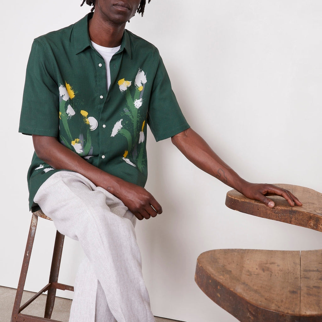 Officine Générale – Chemise Eloi Manches Courtes - Vert Pin/Vert Laitue/Gris - Homme, mannequin homme assis, chemise verte à fleurs, pantalon clair